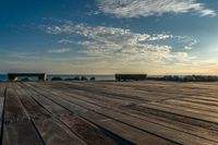 an empty wooden deck overlooking the ocean on a sunny day with the sun setting behind