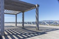 a bench sits under the shade on the pier, overlooking the water and mountains in the distance