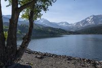 a bench in front of a lake on the side of the road near mountains and trees