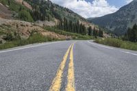 a car is driving down a paved road in the mountains with trees on either side