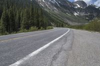 a road in the middle of the mountains that runs from pine to snow topped peaks