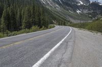 a road in the middle of the mountains that runs from pine to snow topped peaks