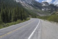 a road in the middle of the mountains that runs from pine to snow topped peaks