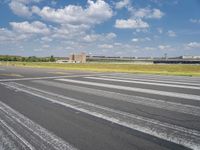 an empty runway surrounded by trees and blue skies and clouds with small buildings along it