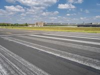 an empty runway surrounded by trees and blue skies and clouds with small buildings along it