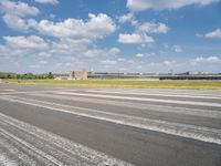 an empty runway surrounded by trees and blue skies and clouds with small buildings along it