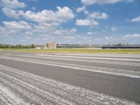 an empty runway surrounded by trees and blue skies and clouds with small buildings along it