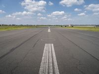 an empty runway with two circles in the middle of it with blue skies and clouds above