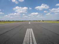 an empty runway with two circles in the middle of it with blue skies and clouds above