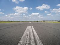 an empty runway with two circles in the middle of it with blue skies and clouds above