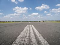 an empty runway with two circles in the middle of it with blue skies and clouds above