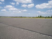 an airport runway and an airfield with lots of grass and clouds in the sky on a sunny day