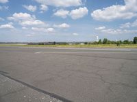 an airport runway and an airfield with lots of grass and clouds in the sky on a sunny day