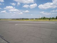 an airport runway and an airfield with lots of grass and clouds in the sky on a sunny day