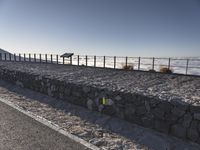 a man walking along the beach on his bicycle near a fence and stone wall, with no people visible