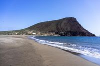 a wide sandy beach with a hill in the background and no cars to the side