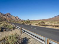 a road goes through a desert landscape with sparse vegetation and mountain peaks and a fence