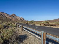 a road goes through a desert landscape with sparse vegetation and mountain peaks and a fence