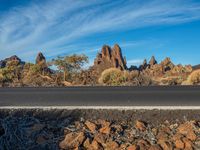 a motorcycle parked by the side of a desert road near some rocks and trees with a few people standing near by