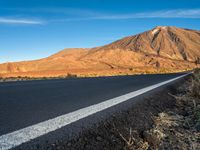 an empty road and the mountains in the background at sunset with a white line on the road