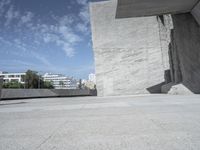 a man on a skate board in a parking lot by a concrete wall and city buildings