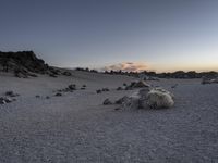 a dirt ground with some rocks and a few clouds in the background at sunset,