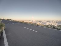 an empty road winds its way up the side of a mountain, with fluffy white clouds