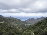 the ocean is seen from behind the green hills and below the clouds in the distance