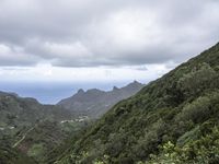 the ocean is seen from behind the green hills and below the clouds in the distance