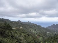 the ocean is seen from behind the green hills and below the clouds in the distance