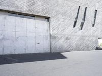 a skate boarder does tricks in front of an industrial building with windows and concrete clad walls