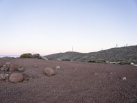 a brown dirt hill with rocks and grass in it and many white buildings on the horizon