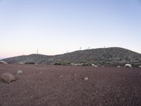 a brown dirt hill with rocks and grass in it and many white buildings on the horizon