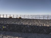 the person is posing on a rocky ledge overlooking the clouds and mountains near a fence