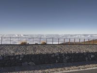 the person is posing on a rocky ledge overlooking the clouds and mountains near a fence