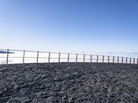 a person standing on top of a black rocky hill under a blue sky on the edge of a cliff