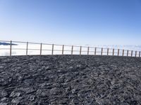 a person standing on top of a black rocky hill under a blue sky on the edge of a cliff