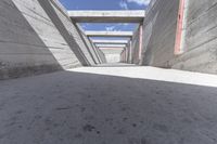 an under construction walkway in cement with red windows and bars above it with a blue sky in the background