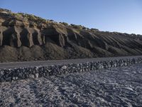 a large mountain covered in gravel and rocks next to a paved road with rocks on both sides and an ocean