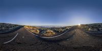 the sun sets over a mountain range on a curved road with two white lines painted on it