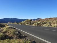 a winding mountain road next to a rocky hill and shrubs in the desert area of arizona