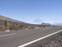 a road near the mountain side in the foggy sun day, and on the opposite bank are hills