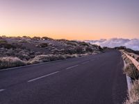 an empty winding road on a mountain with the sun set above the mountains in the background