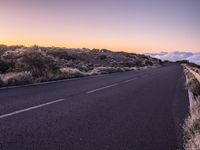 an empty winding road on a mountain with the sun set above the mountains in the background