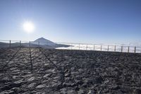 the top of a mountain in front of a fence and mountains with snow on it