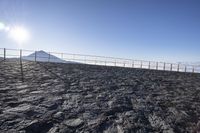 the top of a mountain in front of a fence and mountains with snow on it