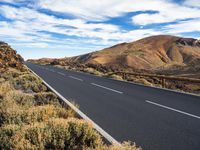 a scenic empty road is shown against the blue sky, with many mountains in the distance