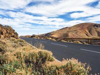 a scenic empty road is shown against the blue sky, with many mountains in the distance