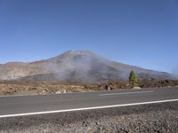 a road near the mountain side in the foggy sun day, and on the opposite bank are hills