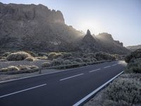 there is a sun setting in the mountains over a road with cars on it and bushes in the foreground